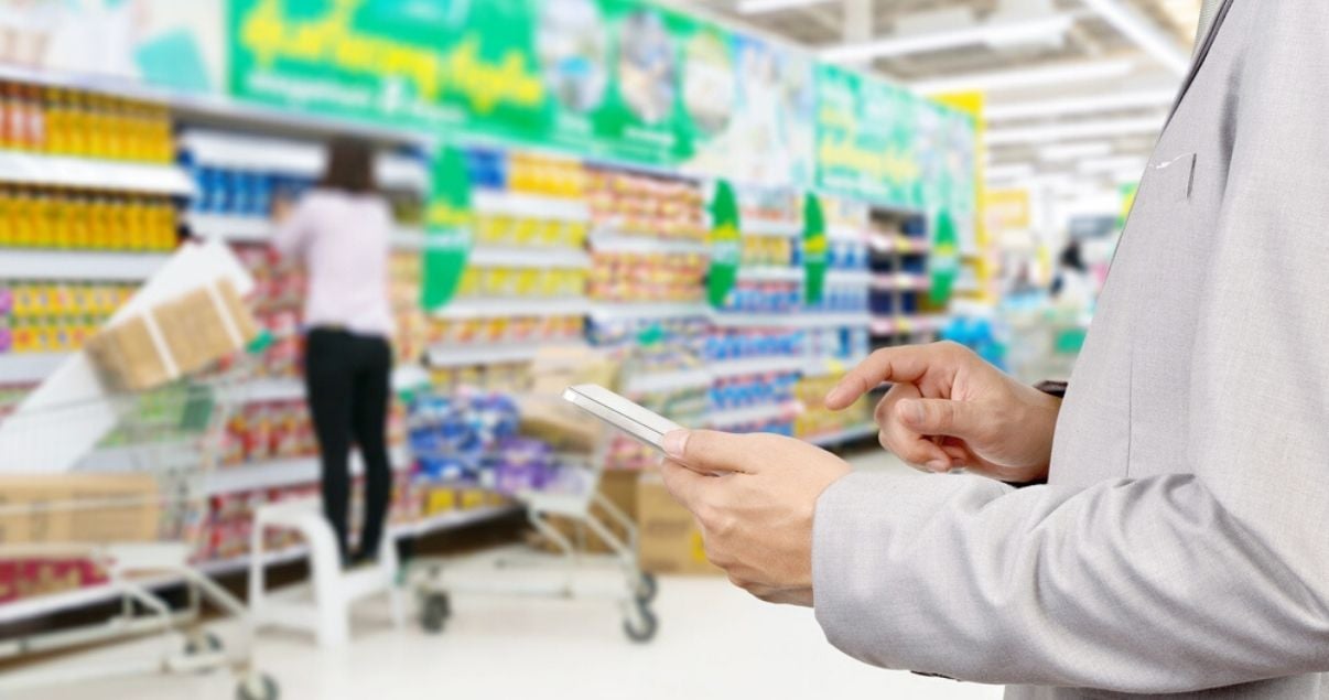 Hombre utilizando un teléfono celular para realizar la auditoría en el punto de venta de un supermercado