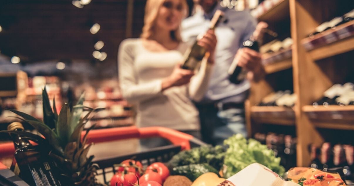 Pareja eligiendo vinos en el putno de venta de un supermercado gracias a las estrategias de trade marketing en distintos tipos de retails